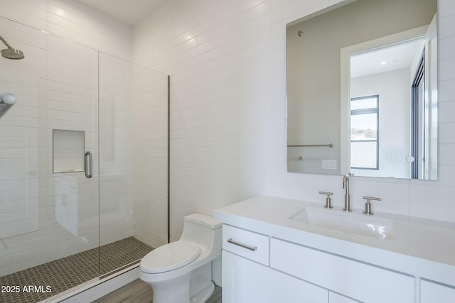 bathroom featuring vanity, toilet, a shower with door, and tile walls