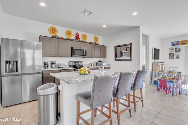 kitchen with sink, light tile patterned floors, a kitchen island with sink, and appliances with stainless steel finishes