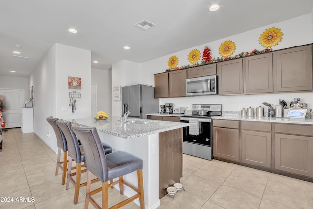 kitchen with light stone countertops, a breakfast bar area, a center island with sink, light tile patterned floors, and appliances with stainless steel finishes