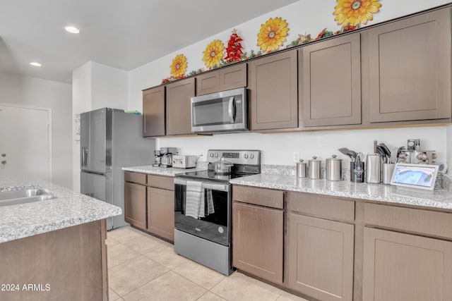 kitchen featuring light stone counters, sink, light tile patterned floors, and stainless steel appliances