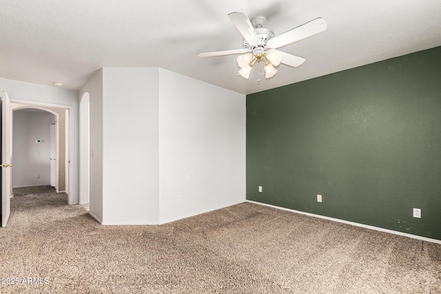 carpeted empty room with arched walkways, ceiling fan, and baseboards
