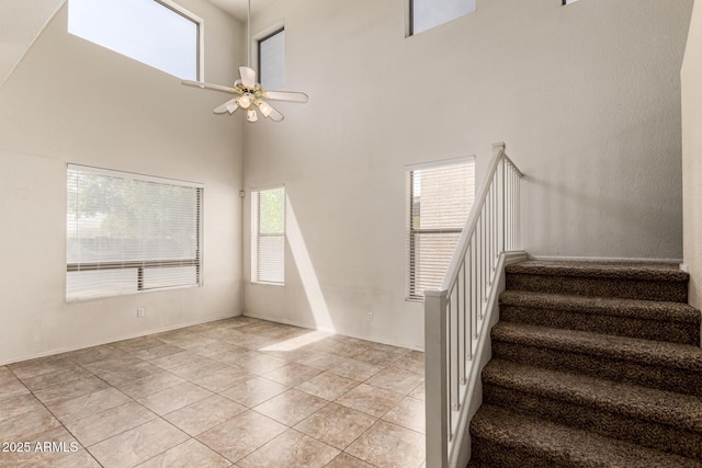 stairway featuring a towering ceiling, tile patterned floors, and ceiling fan