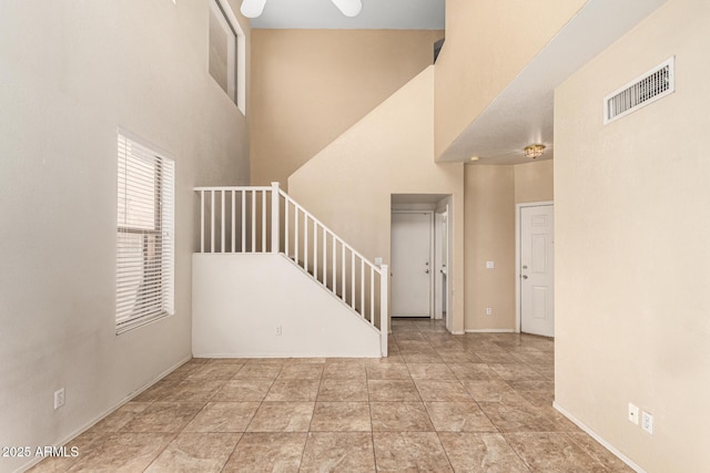 foyer entrance featuring visible vents, stairs, a towering ceiling, baseboards, and a ceiling fan
