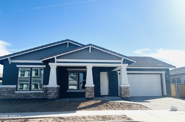 craftsman-style home featuring a garage, driveway, stone siding, and a tiled roof