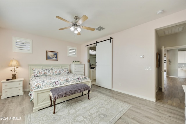 bedroom with ceiling fan, a barn door, and light wood-type flooring