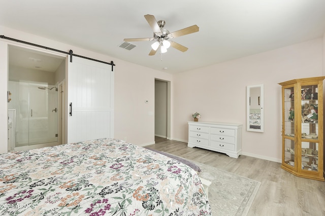 bedroom with a barn door, light hardwood / wood-style floors, ceiling fan, and ensuite bathroom