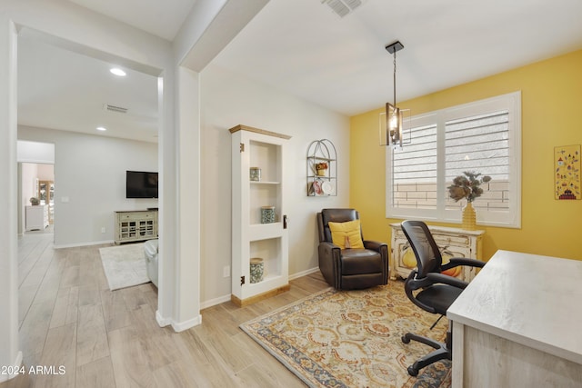 office space with built in shelves, light hardwood / wood-style floors, and an inviting chandelier