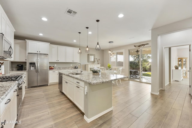 kitchen with pendant lighting, stainless steel appliances, light stone counters, and a kitchen island with sink