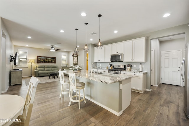 kitchen featuring ceiling fan, hanging light fixtures, stainless steel appliances, a center island with sink, and white cabinets