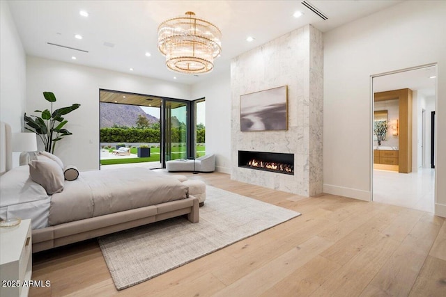 bedroom featuring ensuite bath, light hardwood / wood-style flooring, a fireplace, and a chandelier