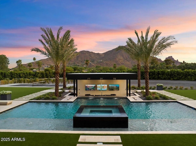 pool at dusk featuring pool water feature, a mountain view, and an in ground hot tub