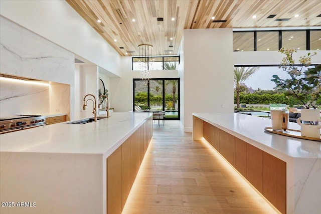 kitchen featuring a large island, sink, wooden ceiling, a high ceiling, and light hardwood / wood-style floors