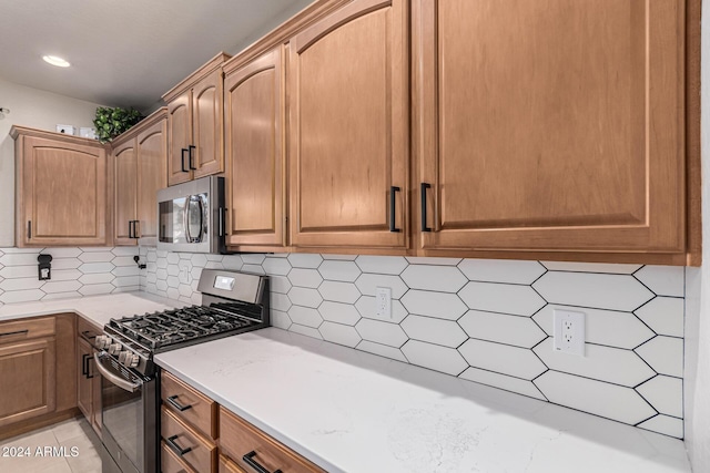 kitchen featuring light stone countertops, stainless steel appliances, light tile patterned floors, and tasteful backsplash