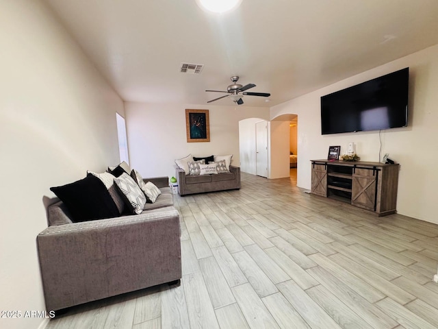 living room featuring arched walkways, visible vents, ceiling fan, and light wood-style floors