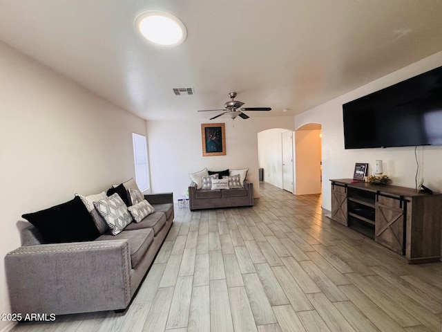 living area with visible vents, arched walkways, light wood-style floors, and a ceiling fan