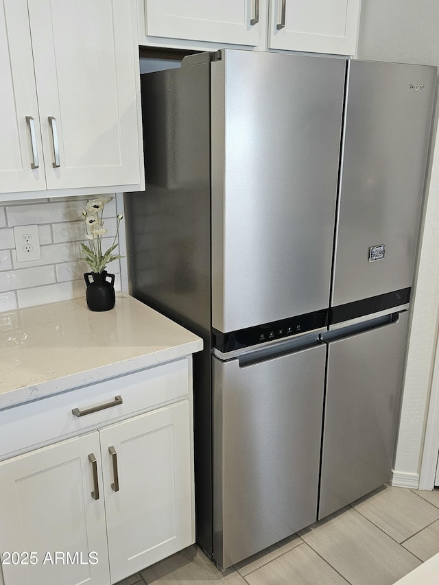 kitchen with white cabinets, freestanding refrigerator, decorative backsplash, and light stone countertops