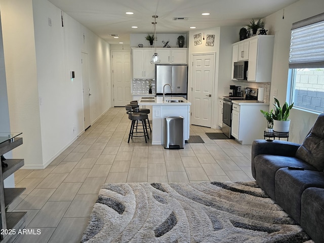 kitchen featuring white cabinets, open floor plan, light countertops, a kitchen bar, and stainless steel appliances