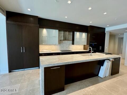 6587 N Palmeraie Blvd Unit 2022, Paradise Valley, AZ 85253 - kitchen with modern cabinets, a large island with sink, wall chimney exhaust hood, decorative backsplash, and light stone countertops