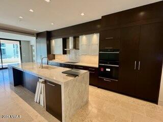 6587 N Palmeraie Blvd Unit 2022, Paradise Valley, AZ 85253 - kitchen featuring wall chimney range hood, modern cabinets, an island with sink, and black appliances