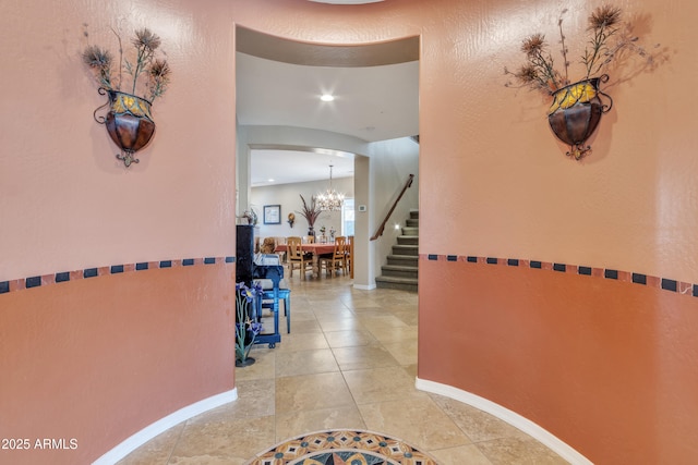 hall featuring arched walkways, a notable chandelier, stairway, tile patterned flooring, and baseboards