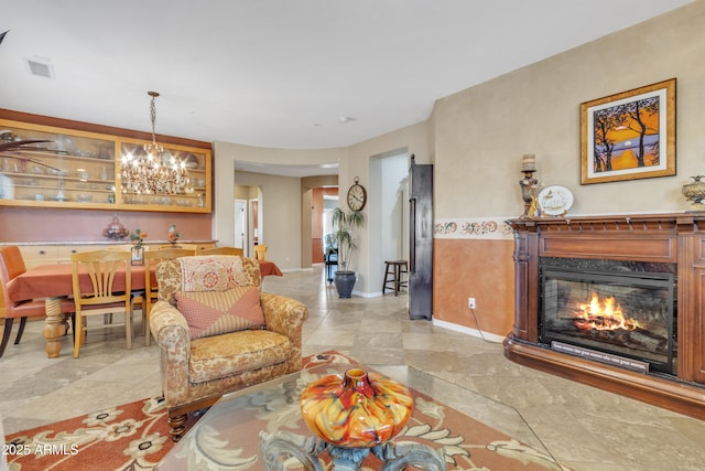 living area with a glass covered fireplace, visible vents, a notable chandelier, and baseboards