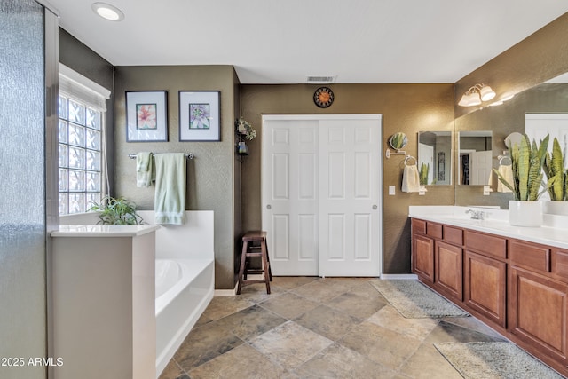 full bath with baseboards, visible vents, a textured wall, a garden tub, and vanity