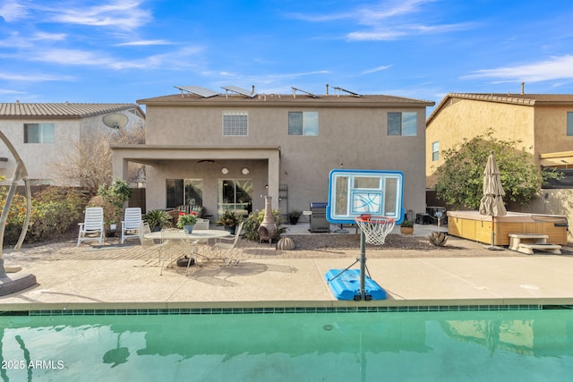 back of property featuring an outdoor pool, a patio, a hot tub, and stucco siding