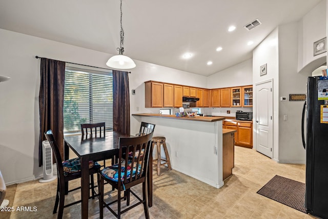 18057 W Port Royale Ln, Surprise, AZ 85388 - kitchen with under cabinet range hood, visible vents, freestanding refrigerator, glass insert cabinets, and brown cabinets
