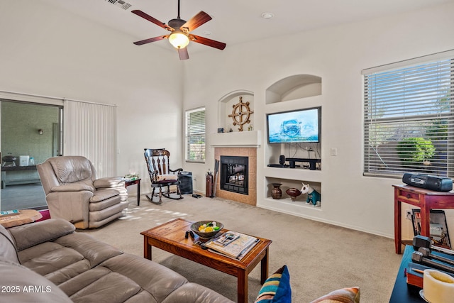 18057 W Port Royale Ln, Surprise, AZ 85388 - carpeted living room with a tiled fireplace, built in shelves, baseboards, visible vents, and ceiling fan