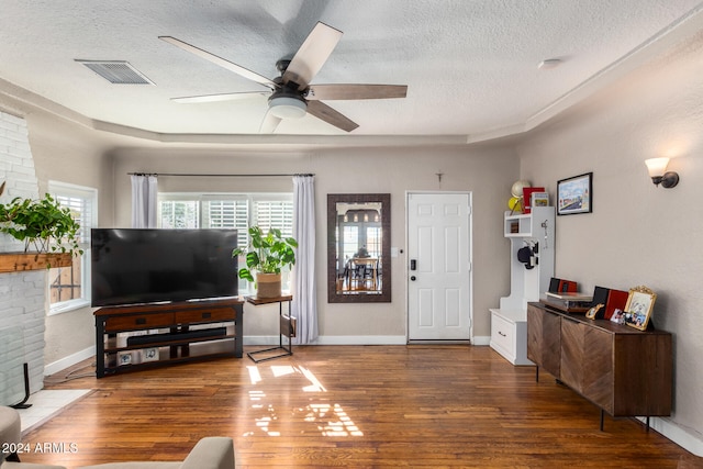 living room featuring a textured ceiling, a fireplace, dark wood-type flooring, and ceiling fan