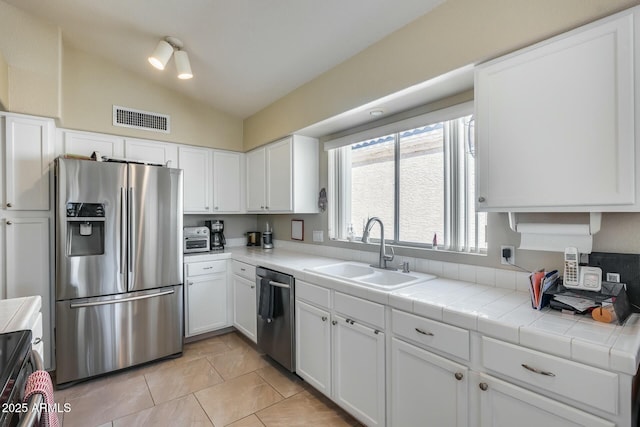 kitchen featuring white cabinetry, lofted ceiling, stainless steel appliances, and tile countertops