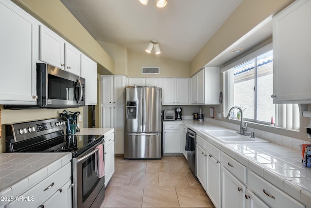 kitchen with sink, tile countertops, vaulted ceiling, and appliances with stainless steel finishes