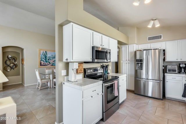 kitchen featuring lofted ceiling, white cabinetry, light tile patterned floors, appliances with stainless steel finishes, and tile counters