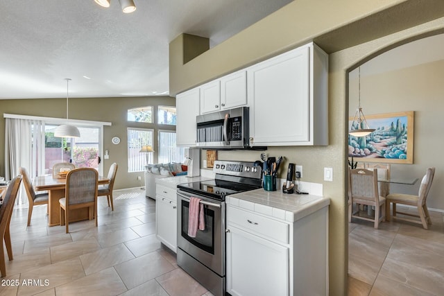 kitchen with lofted ceiling, appliances with stainless steel finishes, tile countertops, and white cabinets