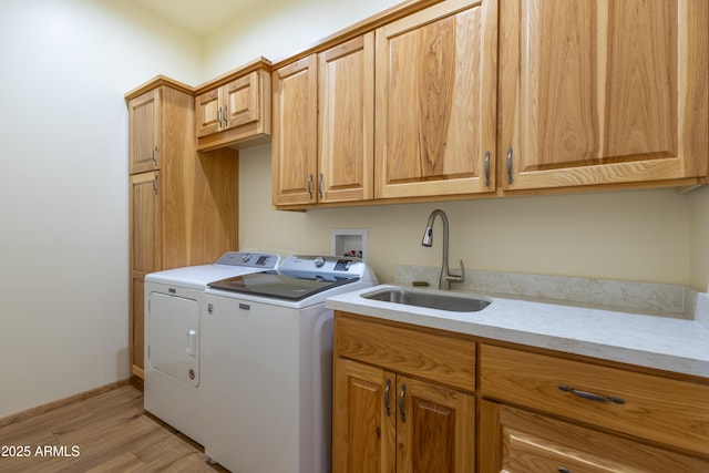 clothes washing area with washing machine and dryer, sink, cabinets, and light wood-type flooring