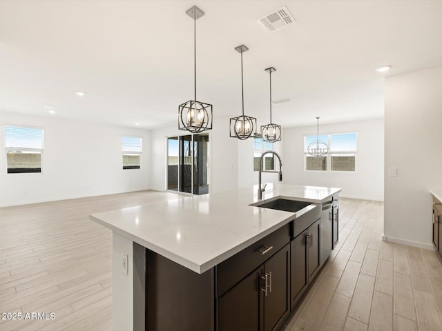 kitchen featuring visible vents, a notable chandelier, a sink, a center island with sink, and light wood-style flooring