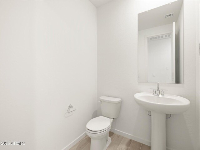 bathroom with toilet, visible vents, baseboards, and wood finish floors