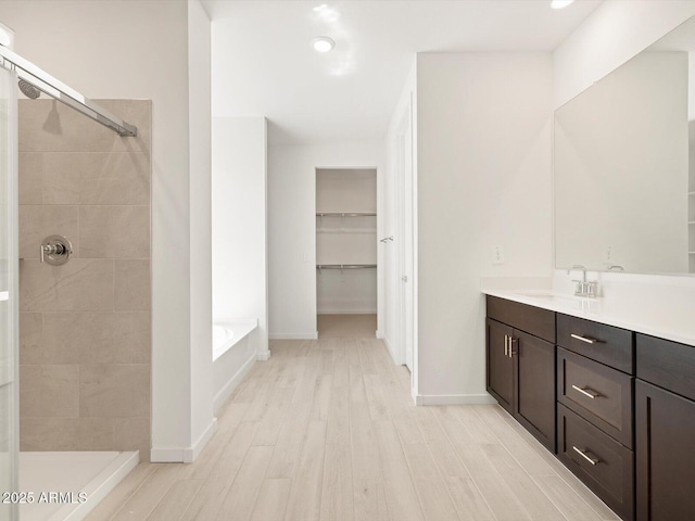 bathroom with a walk in closet, vanity, a tile shower, and wood finished floors