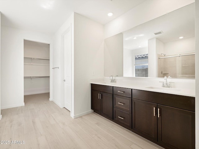 full bath with visible vents, a sink, a stall shower, and wood finished floors