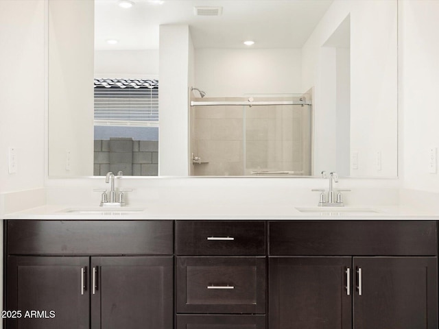 bathroom featuring double vanity, a tile shower, visible vents, and a sink