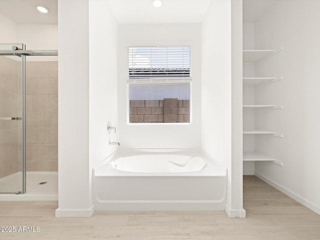 bathroom featuring wood finish floors, a stall shower, baseboards, and a garden tub