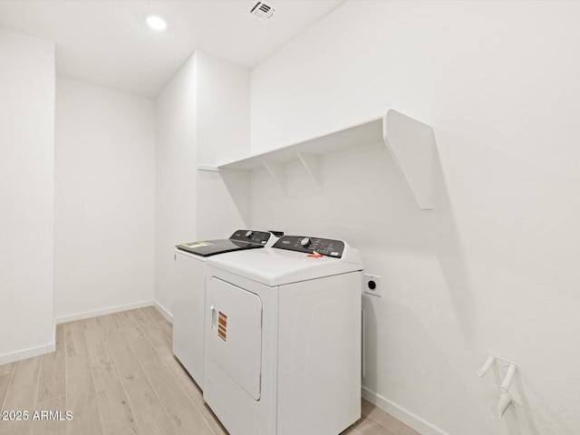 clothes washing area featuring baseboards, light wood-type flooring, visible vents, laundry area, and washing machine and clothes dryer