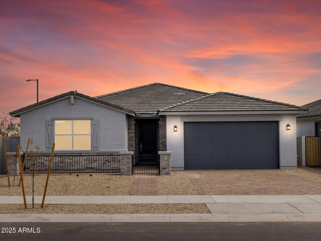 ranch-style home featuring an attached garage, a tile roof, fence, stucco siding, and decorative driveway