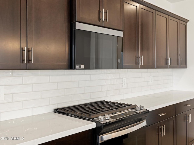 kitchen with stainless steel microwave, tasteful backsplash, light stone counters, dark brown cabinets, and gas range