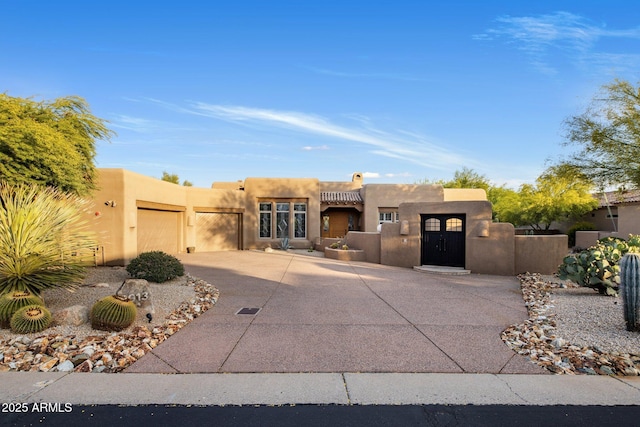 pueblo-style house featuring an attached garage, stucco siding, a gate, fence private yard, and driveway