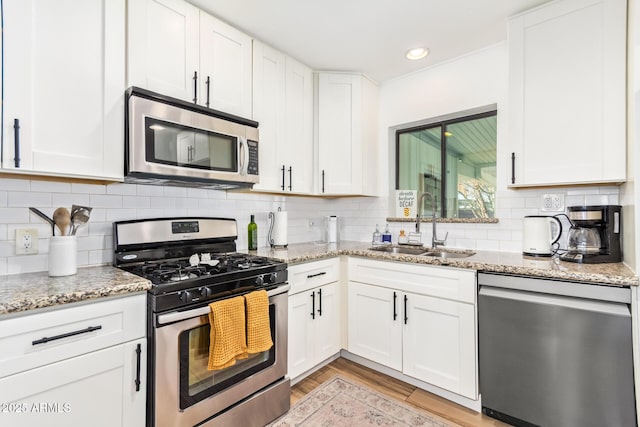 kitchen featuring white cabinets, light wood-style flooring, appliances with stainless steel finishes, a sink, and backsplash