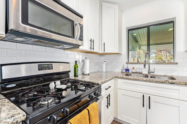 kitchen with decorative backsplash, white cabinets, stainless steel appliances, a sink, and light stone counters