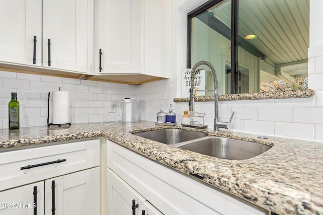 kitchen with white cabinetry, a sink, backsplash, and light stone counters