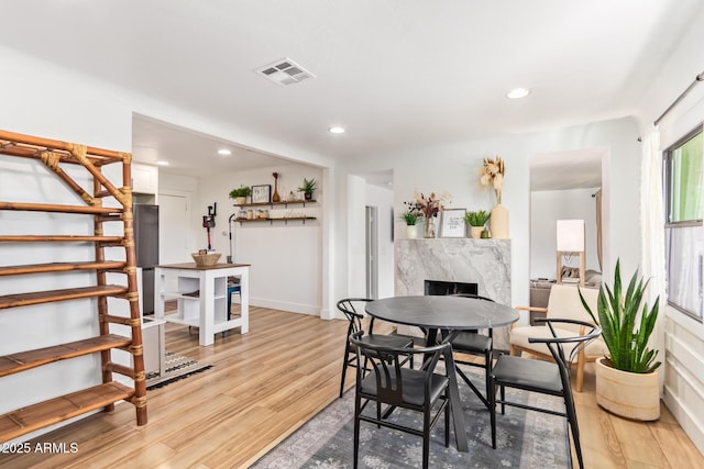 dining space featuring visible vents, light wood-style flooring, stairs, a fireplace, and recessed lighting