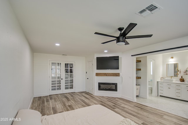 bedroom with french doors, connected bathroom, and light hardwood / wood-style flooring